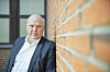 Jan Gunnar Madsen står ved en murvegg i mørk dress og hvit skjorte.