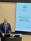 En mann står ved en skjerm med tekst om 130 000 nye boliger og regjeringens plan for Norge.