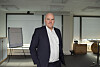 En mann i dress står i et lyst kontorrom med glassvegger og whiteboard.