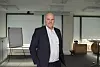 En mann i dress står i et lyst kontorrom med glassvegger og whiteboard.